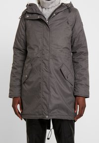 Giubbotto a compressione grigio con zip anteriore, cappuccio regolabile e due tasche laterali con chiusura a scatto. Presenta un tessuto testurizzato e una morbida fodera interna.