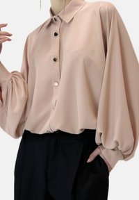 Lichtroze blouse met een kraag, grote pofmouwen en zes zwarte knopen over de voorkant. Gladde stof met een subtiele glans.