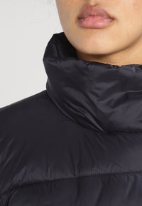 Sort dunjakke med høj krave, der har en glat, blank tekstur og quiltet design, med fokus på varme og komfort.