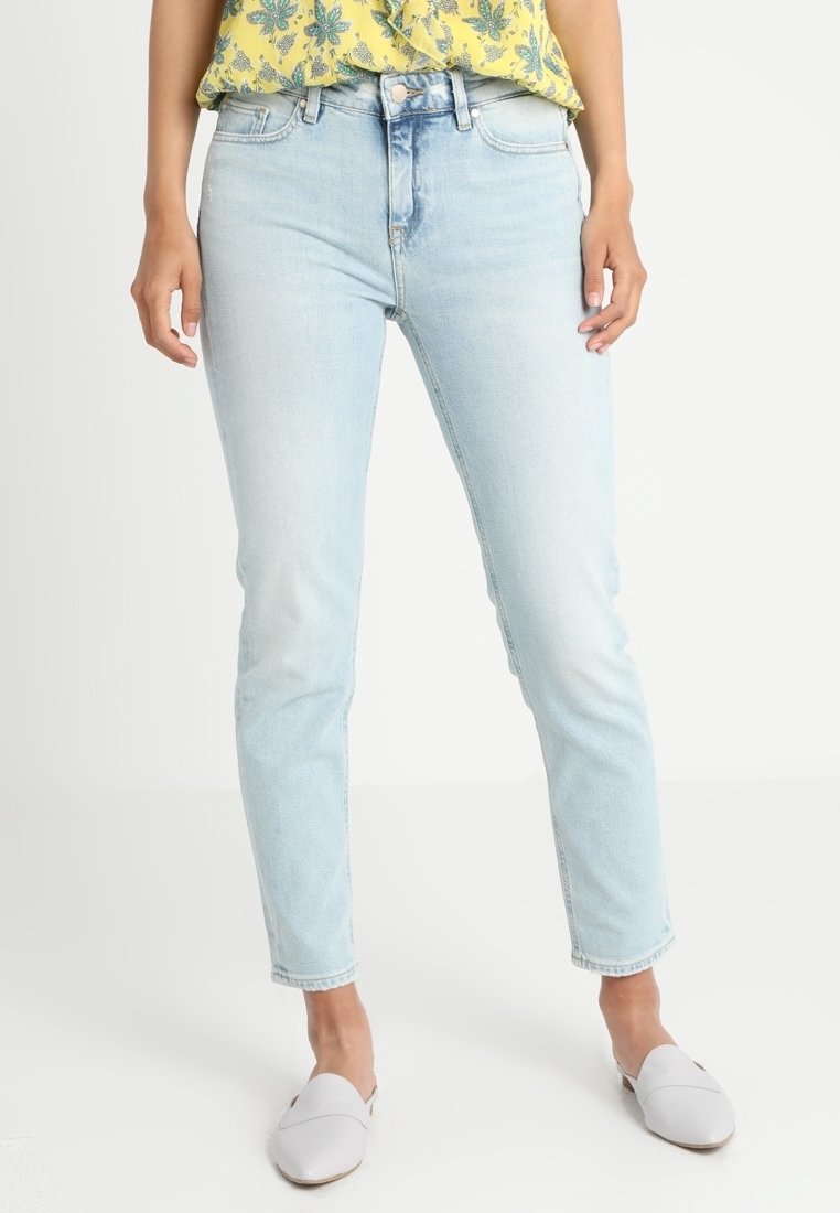 Jean bleu clair à coupe slim, avec une taille haute, un design à cinq poches et des détails légèrement délavés. Associé à un haut jaune à motifs.