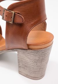 Sandale en cuir marron avec un épais talon bloc texturé et une sangle réglable avec boucle en métal.