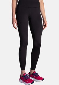 Leggings atletici neri con un design aderente, texture liscia e una tasca laterale. Abbinati a scarpe da corsa rosa brillante con dettagli blu navy.