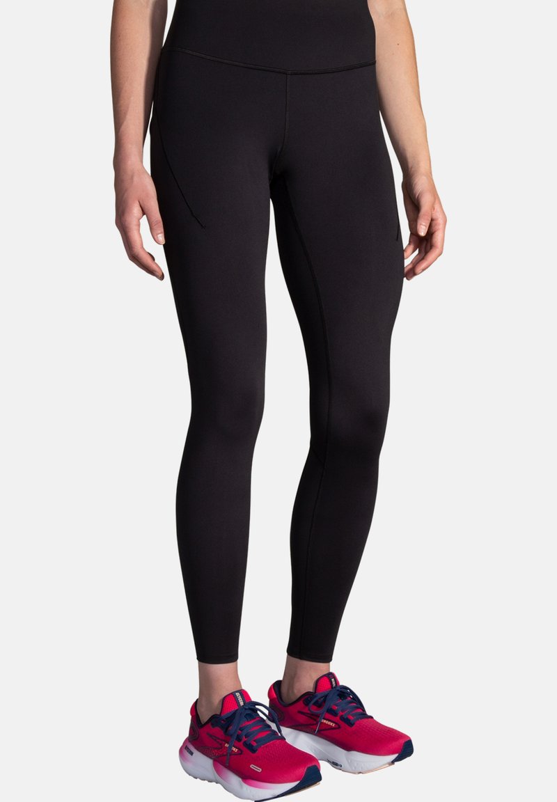 Leggings atletici neri con un design aderente, texture liscia e una tasca laterale. Abbinati a scarpe da corsa rosa brillante con dettagli blu navy.