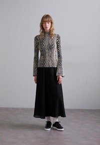 Dlouhý rukáv top s černo-bílým zigzag vzorem, spárovaný s černou plisovanou sukní. Oblečení doplňují černé tenisky.