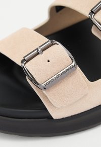 Beige semsket sandal med bred rem, sølvspenne og svart gummisåle. Har preget logo på spennen.