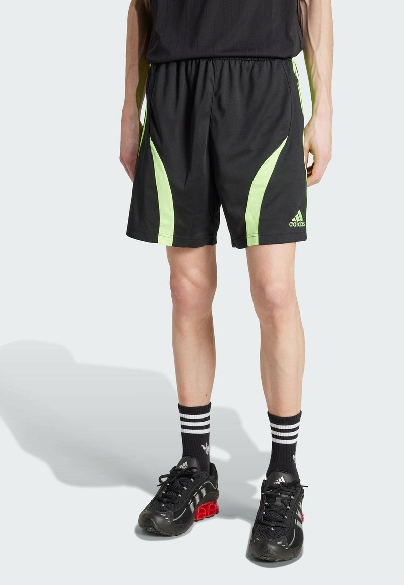 Černé sportovní kraťasy se zelenými bočními akcenty, elastickým pasem a malým bílým logem Adidas na přední straně. Noseny s černými ponožkami a obuví.