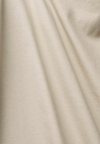 Tissu beige lisse avec de doux plis créant des ombres subtiles et une texture sur la surface.