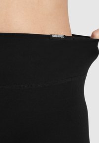 Leggings neri realizzati in tessuto elastico, con una trama liscia, una vita alta e un piccolo etichetta con il marchio sulla parte posteriore.