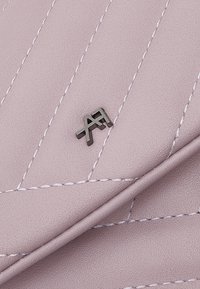 Różowy materiał z sztucznej skóry ze ściegowanym wzorem w diamenty, z metalicznym akcentem w postaci logo. Gładka tekstura i złożony design.