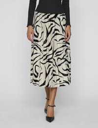 jupe midi plissée en crème avec des rayures abstraites noires ; dotée d'une taille élastique et d'une texture lisse ; accompagnée de chaussures noires à bouts pointus.