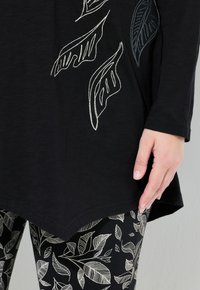 Zwart langarm T-shirt met witte en blauwe bladeren borduursels, gecombineerd met zwarte leggings met witte bladerenpatronen. Zachte, gestructureerde stof.
