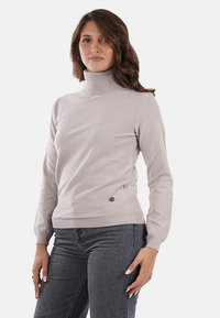 Maglione a collo alto grigio chiaro realizzato in un tessuto morbido, con una leggera lucentezza e un emblema decorativo all'anca, con polsini a coste.