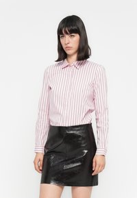 Gestreepte roze overhemd met lange mouwen, gecombineerd met een glanzende zwarte minirok. Het shirt heeft witte en donkerroze strepen.