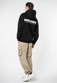 Black hoodie with white text on the back, beige cargo pants, and white sneakers. The hoodie features a kangaroo pocket and ribbed cuffs.