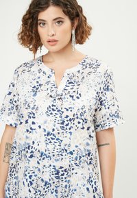 Blusa leggera a maniche corte con base bianca e fantasie astratte blu. Presenta un colletto a scollo a V e un fit morbido. Texture liscia.