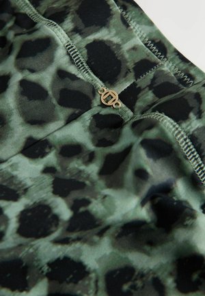 Vihreä-musta eläinkuosinen kangas, jossa on sileä pinta, pieni kultainen logo ja kontrastiväriset tikit saumoissa.