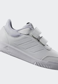 Baskets blanches avec une tige en cuir, accents texturés, deux straps Velcro et trois bandes tonales sur le côté, conçues pour le confort.