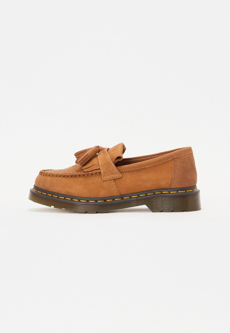Brown suede loafers with a tasseled bow accent, featuring a rounded toe and a thick, ridged sole with orange stitching detail.