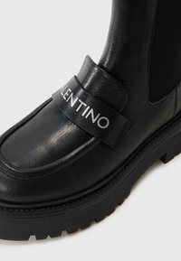 Black leather ankle boot with textured finish, featuring a wide band marked "VALENTINO" and a rugged rubber sole for traction.