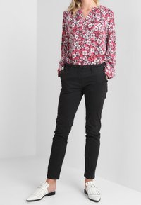 Floral blouse in pink, white, and green; long sleeves with button cuffs. Black fitted pants and white loafers with vertical stripe detailing.