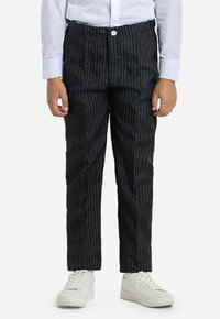 Pantaloni neri a righe sottili con chiusura a bottone e vita elasticizzata, abbinati a sneakers bianche. Tessuto dalla texture liscia e vestibilità su misura.