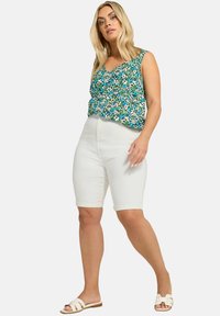 Top sin mangas floral en verde con detalles en azul, blanco y rosa; combinado con pantalones cortos blancos ajustados hasta la rodilla y sandalias ligeras.