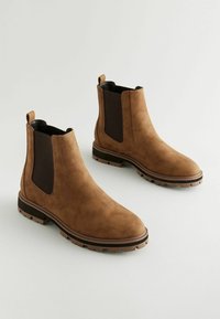 Botas Chelsea de ante marrón con paneles laterales elásticos, tiradores y suelas de goma texturizada y resistente. Diseño clásico con un toque moderno.