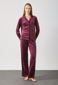 Mørkerød velour pyjamas sættet består af en skjorte med knaplukning, krave og lange ærmer, som matcher lange bukser. Blød tekstur og afslappet pasform.