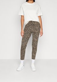 Pantalon en tissu imprimé léopard, coupe ajustée, avec une ceinture élastique et une longueur cheville, associé à un t-shirt blanc et des baskets blanches.