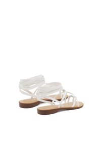 Sandali bianchi a strappo con suole piatte, caratterizzati da un design semplice e un dettaglio decorato sugli strappi. Soletta in tessuto marrone chiaro con texture.