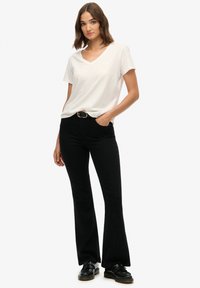 Witte V-hals T-shirt gecombineerd met hoogwater zwarte wijde jeans, voorzien van een riem met een ronde gesp. Klassiek schoeisel maakt de look af.