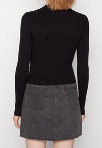 Schwarzes geripptes Langarmoberteil kombiniert mit einem grauen Denimrock, der über Taschen auf der Rückseite und subtile Nähtdetails verfügt.