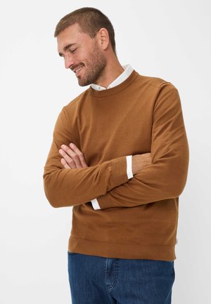 Bruine ronde hals trui met lange mouwen, geribde manchetten en zoom. Draagt over een witte blouse met kraag, gecombineerd met blauwe spijkerbroek.