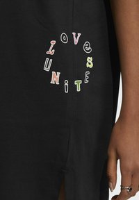 Abito nero con spacco laterale, caratterizzato da testo ricamato multicolore: "AMORE" e "UNISCI" in lettere giocose attorno a un design circolare.
