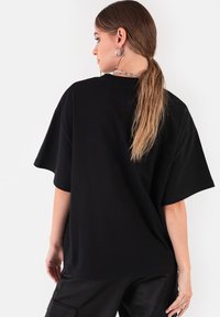 Czarna, oversize koszulka wykonana z bawełny, z krótkimi rękawami i okrągłym dekoltem. Tył ma gładkie wykończenie z luźnym krojem.