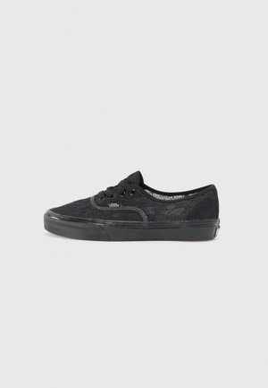 Zapatilla baja negra Vans con superposición de encaje, suela de goma negra y cinco ojales para cordones, mostrada de perfil sobre un fondo liso.