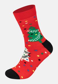 Red socks with a green Christmas tree, "Happy Holidays" text, and colorful polka dots; black accents at the toe and heel.