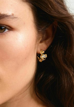 Boucles d'oreilles en or en forme de créoles avec un design texturé, ornées de rhinestones transparents disposés en arrangement floral. Le matériau semble poli.