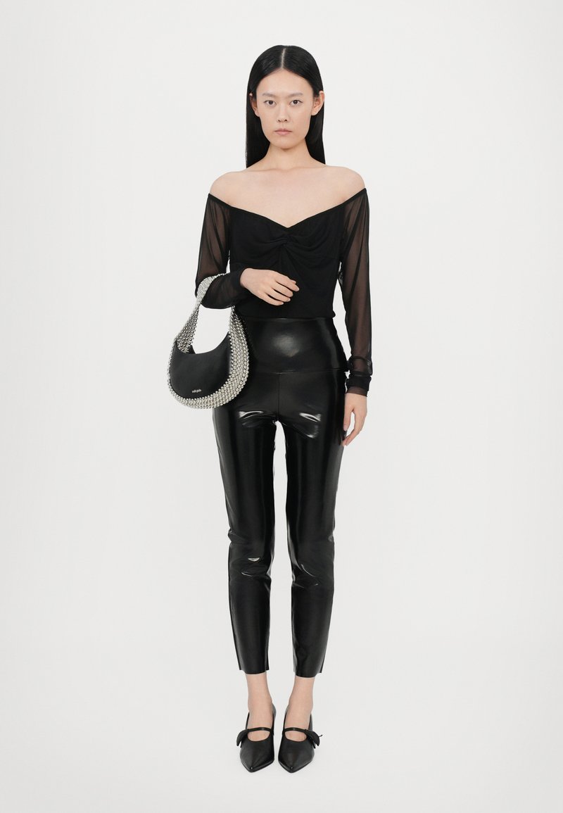 Top nero senza spalle con dettagli arricciati, abbinato a pantaloni neri in ecopelle lucida. La modella tiene una borsa nera con dettagli argento.