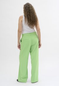 Groene wijde broek met een soepele textuur, voorzien van riemlussen en achterzakken, gecombineerd met een witte mouwloze top.