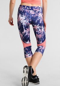 Capri leggings featuring a dark blue tropical palm print with pink accents, made of stretchable fabric, with a mesh panel at the calf.
