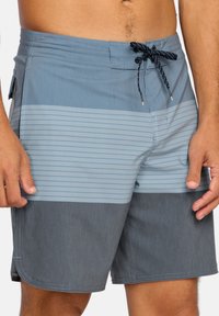 Pánské plavecké šortky s dvoubarevným designem ve modrých odstínech, s vodorovnými pruhy a šňůrkou v pase. Vyrobeno z lehkého materiálu.
