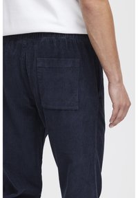 Tmavomodré kordové nohavice s textúrovaným povrchom, s nášitou zadnou vreckou a elastickým pásom, viditeľné z bočného pohľadu.