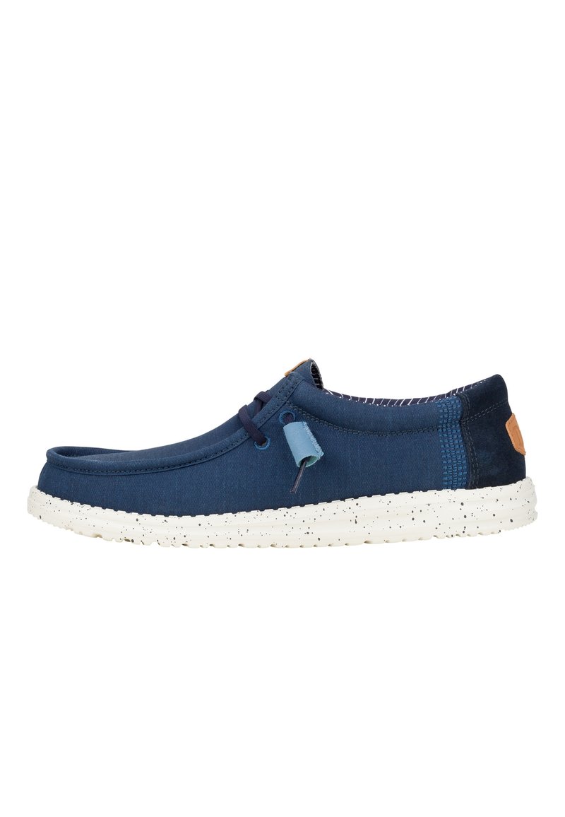 Chaussure en toile marine avec un bout rond, semelle blanche à motifs, lacets décoratifs et accent de languette. Présente un talon et un intérieur en bleu foncé texturé.