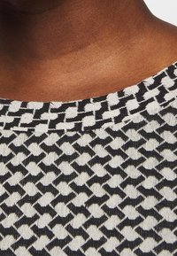 Strickpullover mit einem schwarz-weißen geometrischen Muster und Rundhalsausschnitt. Nahaufnahme zeigt die Stoffstruktur und die Detailansicht des Ausschnitts.