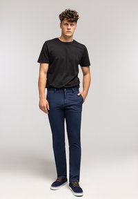 Czarny bawełniany t-shirt, granatowe spodnie o dopasowanym kroju oraz granatowe sneakersy z brązowymi sznurowadłami. Prosty design, dyskretne logo na koszulce.