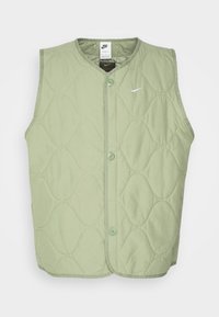 Ljust grönt quiltat ärmlöst väst med tre knappar och en liten vit Nike swoosh-logotyp på bröstet.