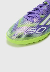 Crampons de football violettes et vertes avec un design rayé, présentant une marque blanche et une surface texturée. Comprend des lacets assortis et une semelle moulée.
