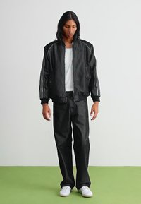 Crna bomber jakna s kontrastnim sivim prugama, zatvarač sprijeda i rebrasti manžeti, uparena s širokim crnim trapericama i bijelim tenisicama.