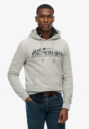 Grijze katoenen hoodie met trekkoord, grote voorzak en "Superdry" logo met berggraphics. Draag over een marineblauwe shirt, gecombineerd met blauwe jeans.